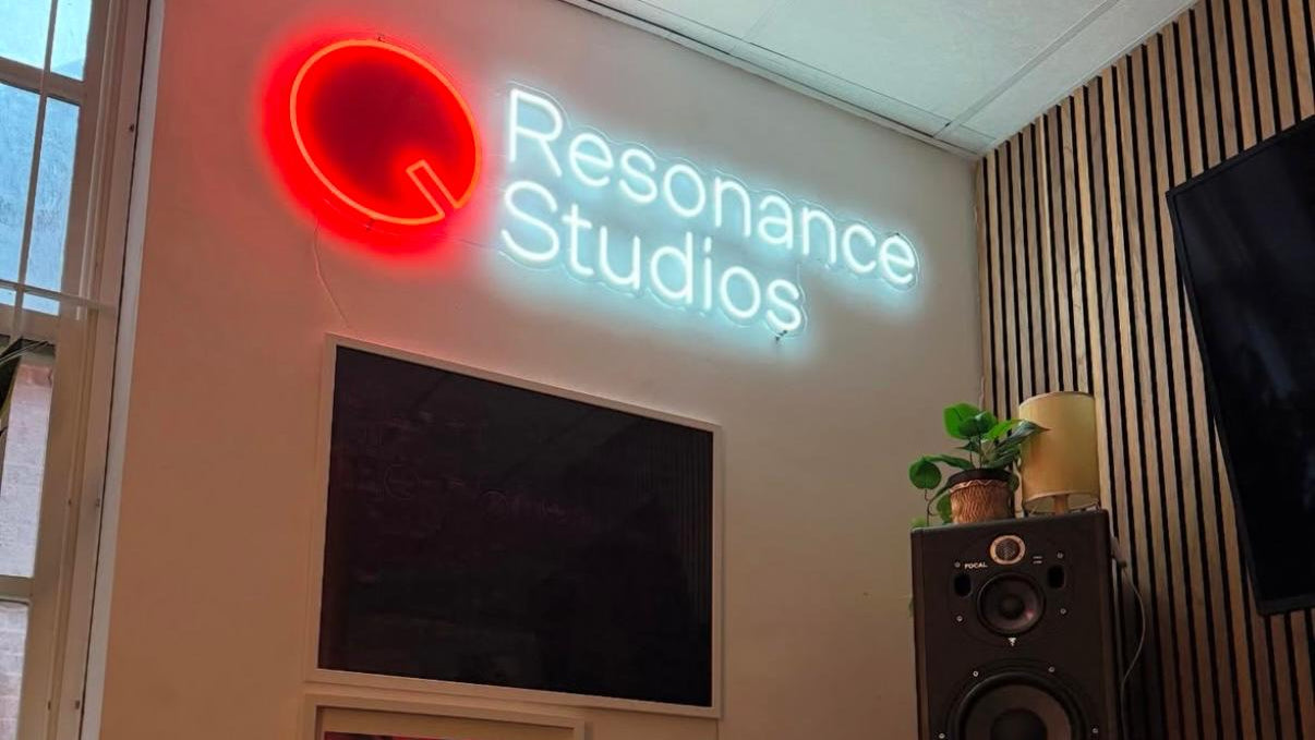 Music studio with a synthesizer, speakers, and 'Resonance Studios' neon sign.